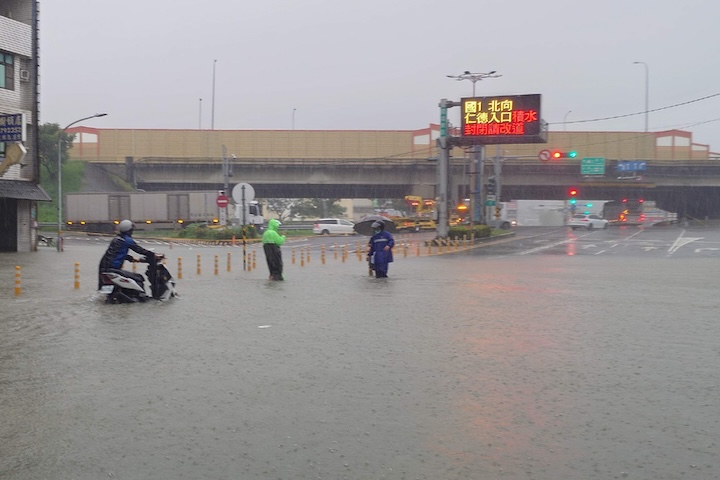 大雨襲台南,國道1號台南仁德交流道周邊23日清晨因雨勢出現積淹水,仁德交流道北向入口一度封閉,有機車騎士牽車勉強涉水通過積水路段。圖/中央社