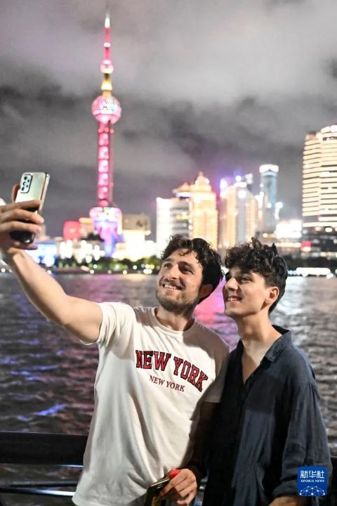 7月18日晚，兩位義大利遊客阿爾弗雷多·奇米諾（左）和朱利奧·巴爾托利在上海外灘與東方明珠合影。圖/取自新華社
