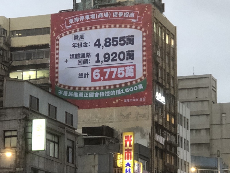 基隆市政府24日在忠一路大樓外牆高掛起巨幅廣告，提到「東岸停車場（商場）促參招商」收入 數據。圖/中央社
