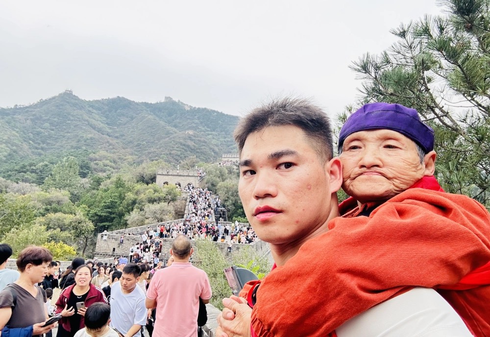 在八達嶺長城上，一位年輕人背著年邁的母親，一步一步小心翼翼地攀登著。圖/取自《北京日報》