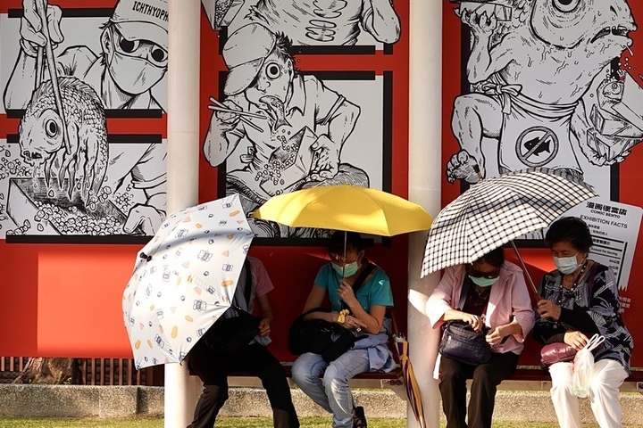 各地天氣高溫炎熱，等待搭乘高雄輕軌的民眾撐傘遮陽。圖/取自中央社