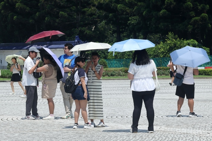 各地天氣高溫炎熱，民眾出遊到台北市中正紀念堂，撐傘避免太陽直接照射。圖/取自中央社